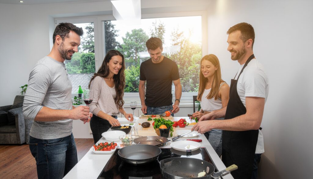 Cinco personas cocinando juntas alrededor de una cocina, en un ambiente agradable y colaborativo, ilustrando la idea de un club gastronómico compartido en Beniaján.”