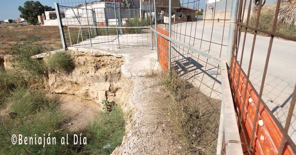 Vista del tramo de acera del Bojar en Beniaján junto al solar de la obra paralizada, donde se observa el hueco dejado por las excavaciones, las vallas perimetrales parcialmente suspendidas y el paso peatonal estrechado.
