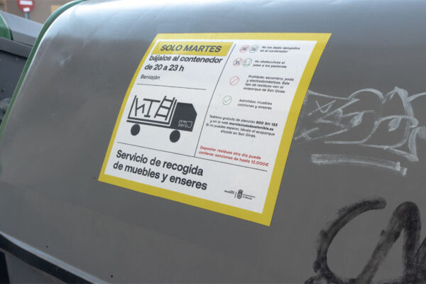 Cartel de aviso con el estricto horario de recogida de muebles y enseres frente a un grupo de contenedores en Beniaján.