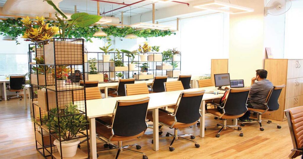 Coworking en Beniaján: espacio diáfano con mesas, plantas y dos personas trabajando en sus ordenadores, mostrando un ambiente agradable y colaborativo