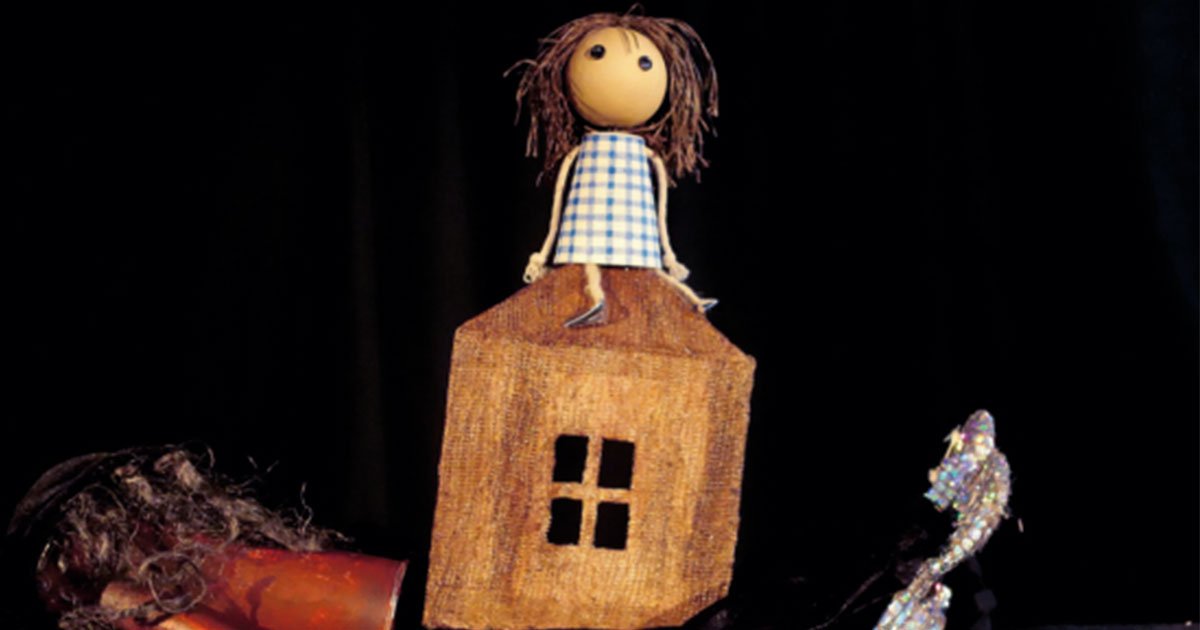 Muñecos y títeres de La Canica Teatro en el Auditorio de Beniaján, con una muñeca sentada en una casita de madera y objetos de utilería sobre fondo negro