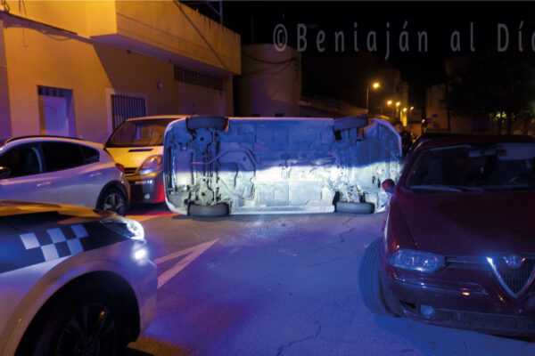 Coche Toyota Auris volcado en la calle Instituto de Beniaján, con otros vehículos aparcados y un coche de la Policía Local presente