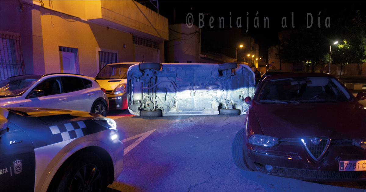 Coche Toyota Auris volcado en la calle Instituto de Beniaján, con otros vehículos aparcados y un coche de la Policía Local presente
