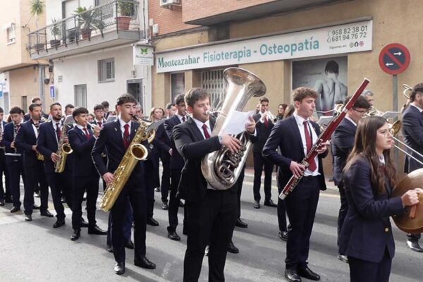 La Escuela de Música de Beniaján desfilando por las calles del pueblo durante la celebración de Santa Cecilia, patrona de la música, con vecinos observando y disfrutando del recorrido.