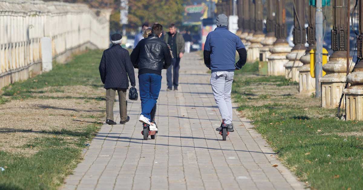 Dos individuos de espaldas circulando con patinetes eléctricos sobre una acera en Beniaján. La imagen ilustra la inacción policial ante el incumplimiento de la normativa de VMP.