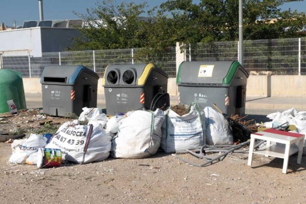 Grupo de contenedores de residuos en un descampado de Murcia, rodeados de bolsas de basura, escombros y restos de construcción, ejemplo de feísmo urbano y contaminación visual.