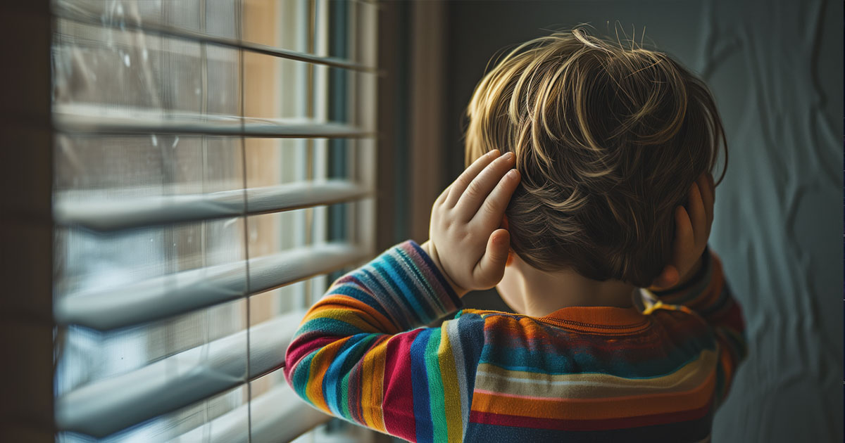 Niño de espaldas con manos en las orejas frente a una ventana, protegiéndose del ruido en Beniaján. La contaminación acústica afecta la salud infantil en las pedanías de Murcia.
