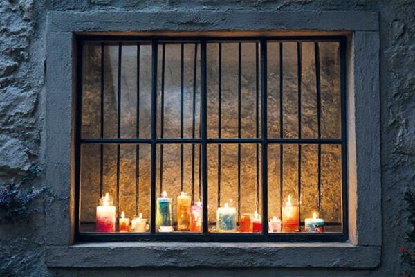 Fachada de edificio antiguo en Beniaján iluminada por múltiples velas de colores durante el evento cultural Beniaján en Vela 2025, con ventana y rejas visibles.