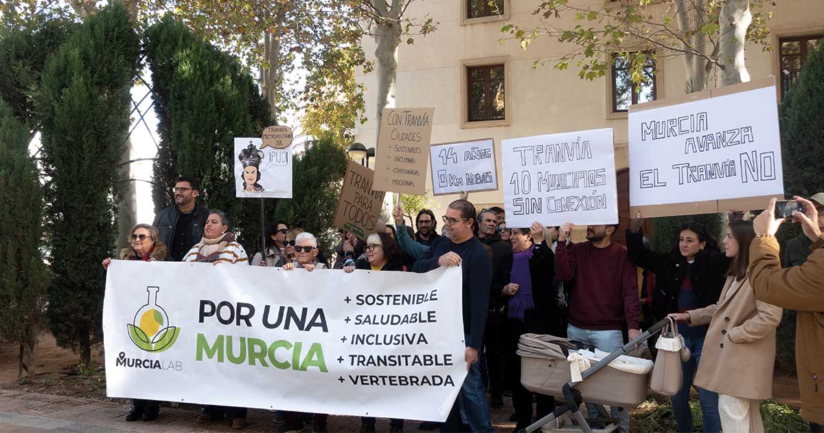 Participantes de MurciaLAB en concentración frente al Palacio de San Esteban el 29 de noviembre, reivindicando un transporte público de calidad y la ampliación del tranvía, con pancarta visible.