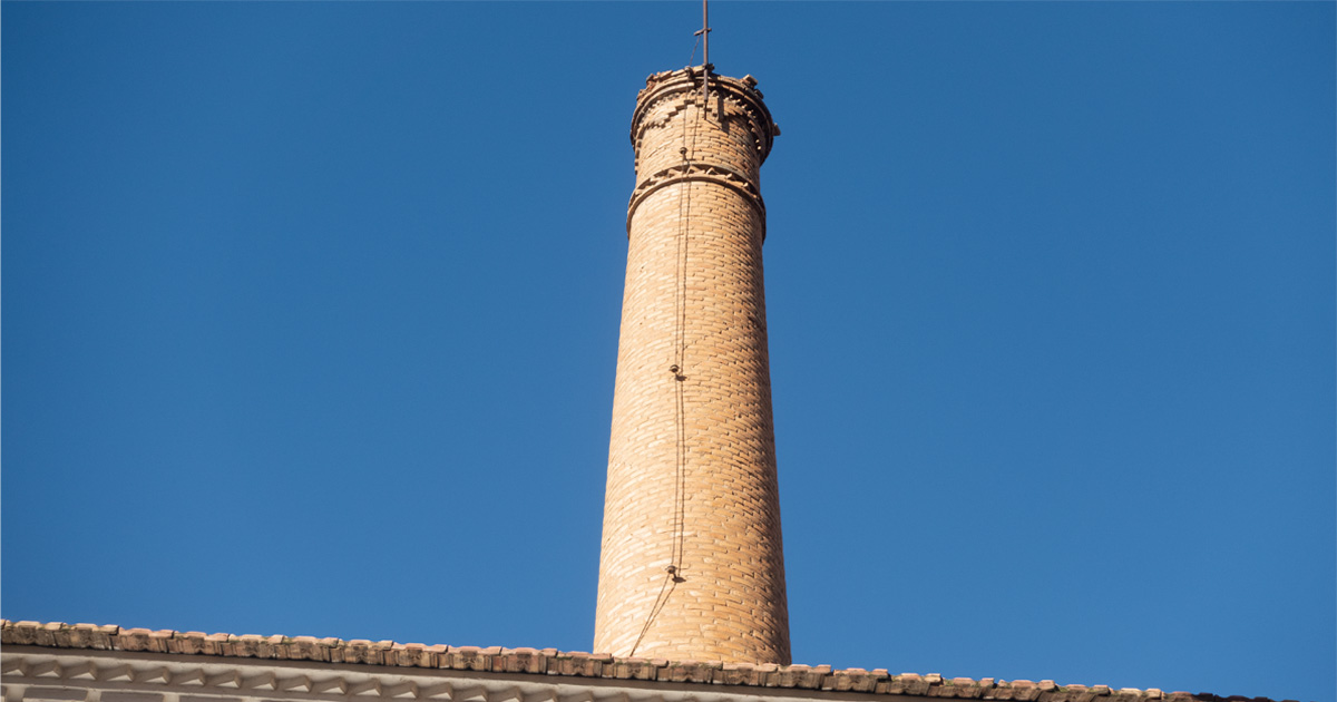 Chimenea industrial protegida en la calle Rambla de Torreagüera, visible sobre el tejado del antiguo edificio, con la boquilla superior deteriorada