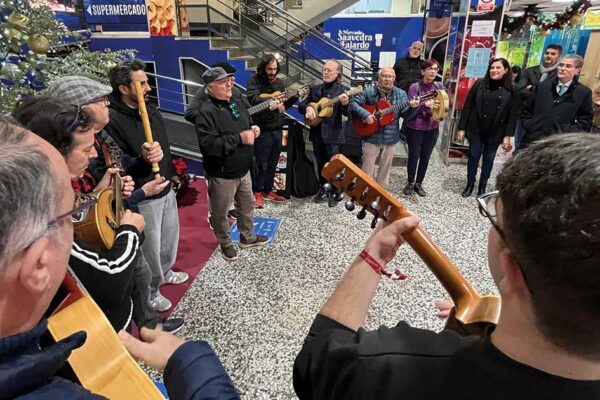 Jóvenes integrantes de una cuadrilla murciana tocando instrumentos y cantando villancicos en una plaza de abastos del centro de Murcia, dinamizando la tradición navideña