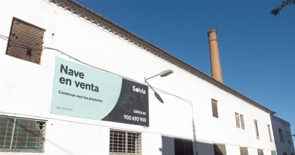 Edificio histórico de la calle Rambla en Torreagüera con la chimenea industrial visible sobre el tejado y un cartel de venta de Solvia en la fachada.