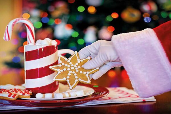 Mano de Santa Claus colocando un adorno navideño sobre una mesa con centros decorativos, ilustrando la Navidad en barrios y pedanías del Ayuntamiento de Murcia.