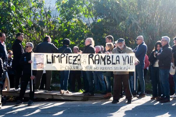 Grupo de asistentes con pancarta y lema en la concentración por la limpieza de la rambla del Garruchal en El Secano, con políticos presentes al fondo.