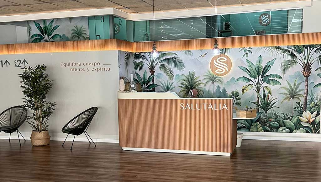 Recepción luminosa de Salutalia en Beniaján: mostrador de entrada con paredes claras, suelo de madera y ambiente abierto y sereno para bienestar holístico.