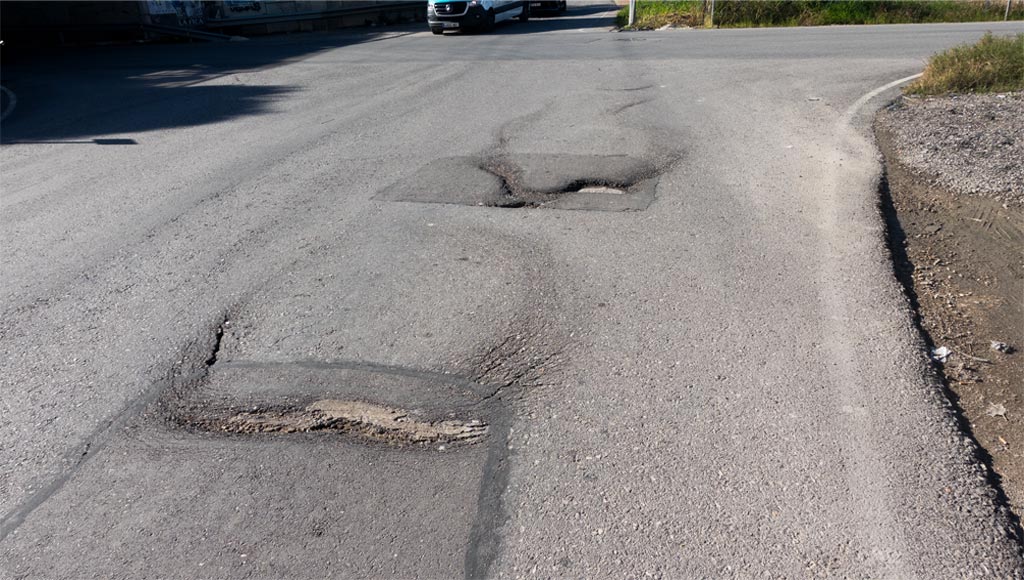 Deterioro del asfalto claramente visible en el cruce del Camino del Embalse, Torreagüera (Murcia): detalle nítido del firme irregular que genera riesgo de accidentes