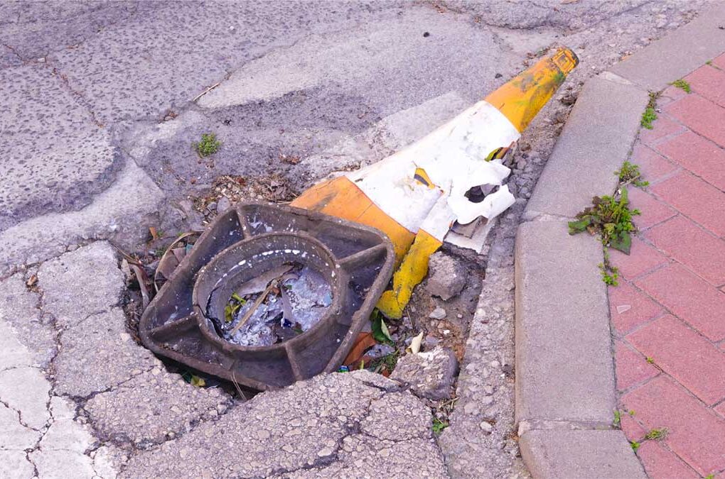 Cono de tráfico aplastado y fusionado con el asfalto junto a una arqueta rota en San José de la Vega (Murcia), símbolo de baches eternos y chapuzas en pedanías