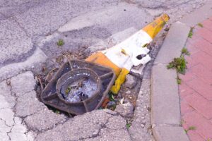 Cono de tráfico aplastado y fusionado con el asfalto junto a una arqueta rota en San José de la Vega (Murcia), símbolo de baches eternos y chapuzas en pedanías