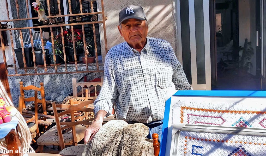 Antonio el Hierros posando en su casa junto a cuadros de ganchillo, redes artesanales y muñecos hechos a mano