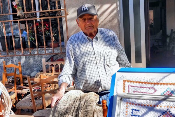 Antonio el Hierros posando en su casa junto a cuadros de ganchillo, redes artesanales y muñecos hechos a mano