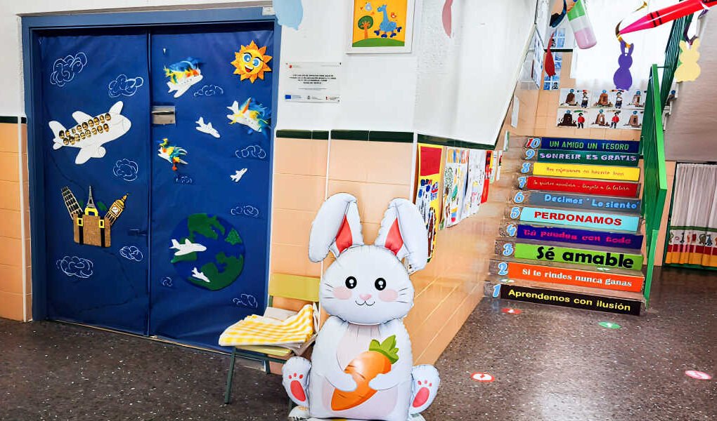 nterior de la Escuela de Educación Infantil La Naranja de Beniaján, con escaleras decoradas con lemas, un conejillo de juguete con zanahoria y la puerta de una aula