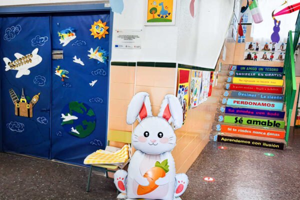 nterior de la Escuela de Educación Infantil La Naranja de Beniaján, con escaleras decoradas con lemas, un conejillo de juguete con zanahoria y la puerta de una aula