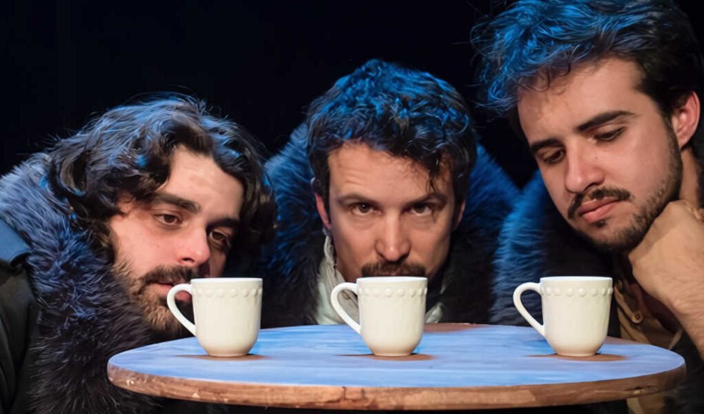 Tres actores en una escena de Las tres hermanas de Antón Chéjov observando tres tazas sobre una mesa