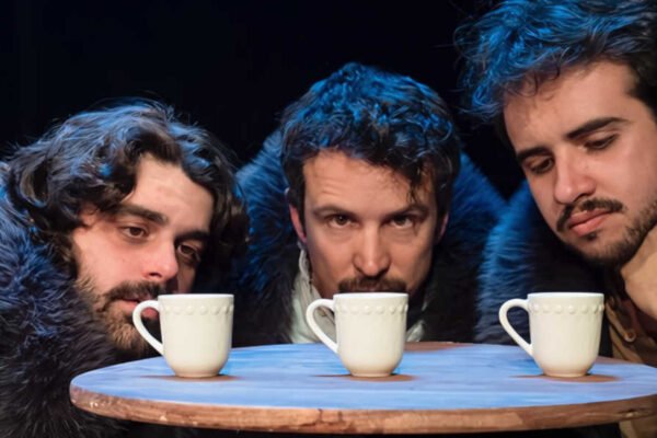 Tres actores en una escena de Las tres hermanas de Antón Chéjov observando tres tazas sobre una mesa