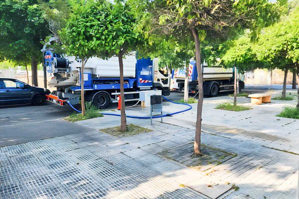 Dos camiones de limpieza viaria cortando la calle José Ortiz García mientras cargan agua en la urbanización Los Naranjos, en Beniaján