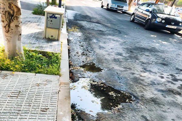 Agua estancada en la calzada junto al punto de carga en la calle José Ortiz García, con deterioro del firme en la urbanización Los Naranjos (Beniaján)
