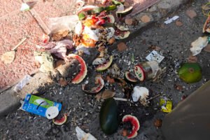 Residuos orgánicos en la acera de Beniaján con restos de sandía, pepino y envases abandonados al sol con presencia de insectos