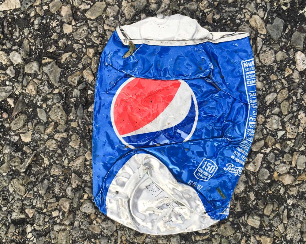 Lata de refresco de aluminio aplastada sobre el suelo, símbolo del reciclaje de envases.