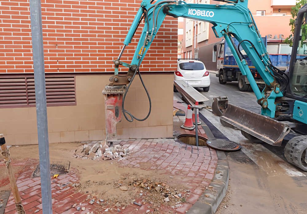 Maquinaria pesada abre una zanja para reparar una rotura en la red general de agua en la calle Federico Giráo de Beniaján.