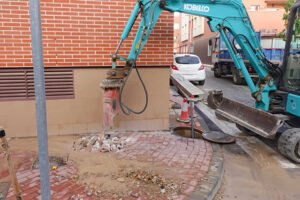 Maquinaria pesada abre una zanja para reparar una rotura en la red general de agua en la calle Federico Giráo de Beniaján.