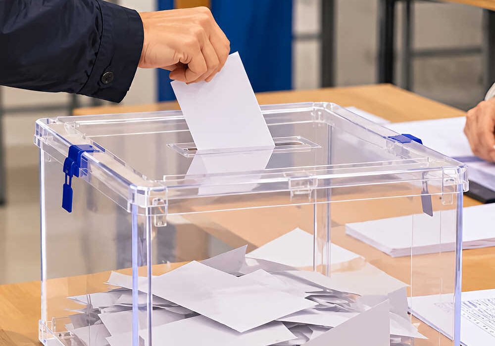 Urna transparente con un ciudadano depositando su voto en una mesa electoral durante las elecciones generales.