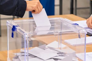 Urna transparente con un ciudadano depositando su voto en una mesa electoral durante las elecciones generales.