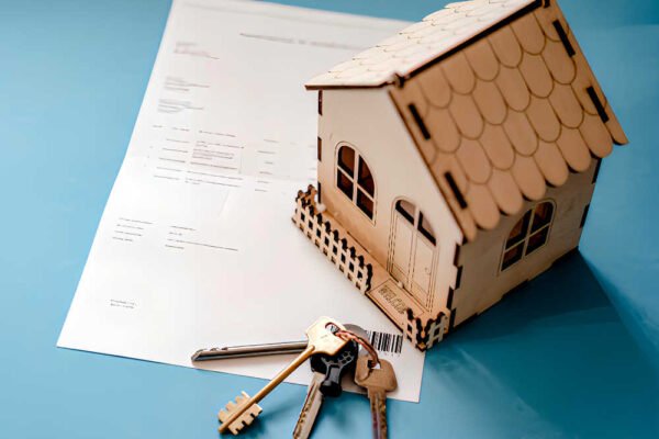 Maqueta de casa de madera, llaves y documento de contrato de alquiler de vivienda sobre fondo azul.