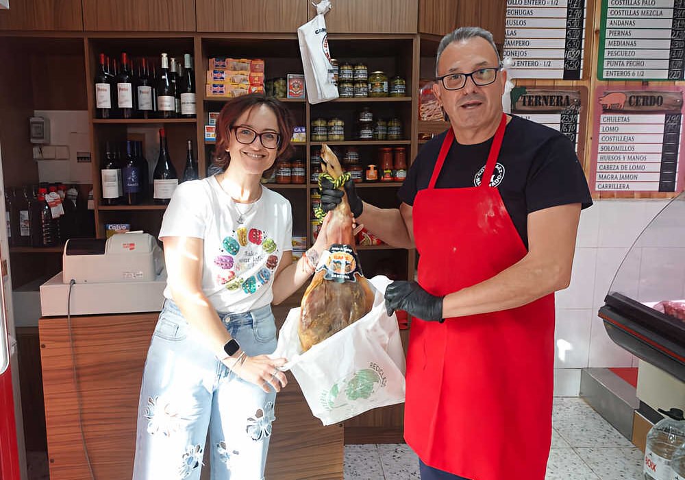 Silvia Suárez Lax recibe el primer jamón sorteado por Beniaján al Día de manos del gerente de la carnicería González Manchado, en Beniaján.