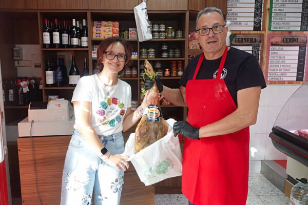 Silvia Suárez Lax recibe el primer jamón sorteado por Beniaján al Día de manos del gerente de la carnicería González Manchado, en Beniaján.