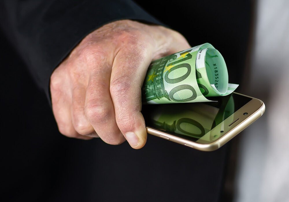 Billete de 100 euros junto a un móvil, en referencia a la devolución del dinero por estafas bancarias online.