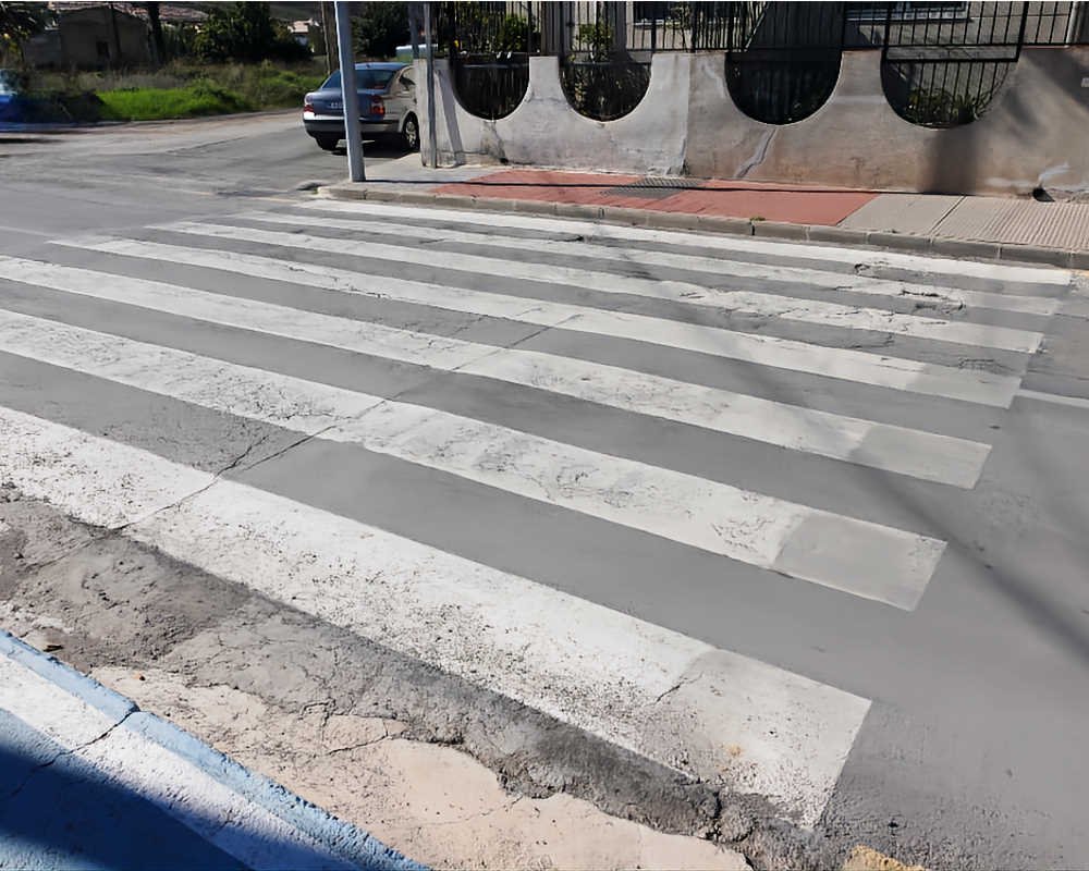 Paso de peatones inaccesible en San José de la Vega (Murcia) con bordillo vertical y calzada deteriorada sin rebaje a cota cero.
