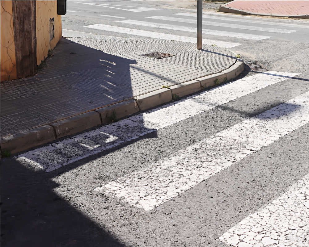 Paso de peatones pintado contra un bordillo curvo sin rebajar en una acera estrecha de San José de la Vega (Murcia).